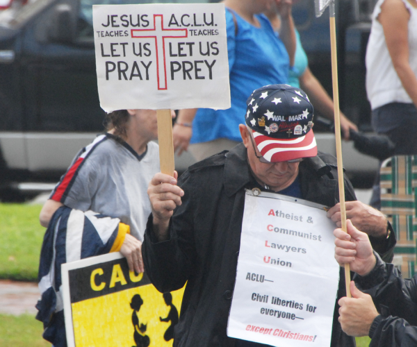 people hold signs, one protester holds 2 calling out the aclu