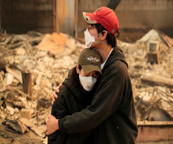 residents of Los Angeles wearing masks, hugging, in front of burned out homes