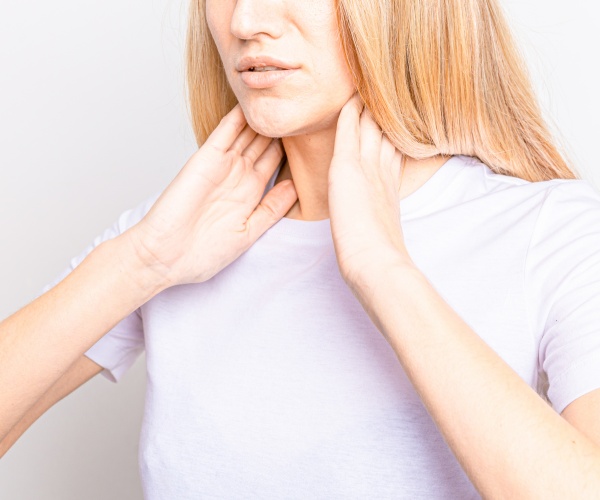 woman holding her neck, checking her thyroid