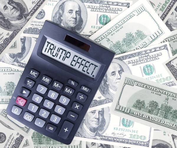 a calculator with trump effect written on it and lying on top of hundred dollar bills