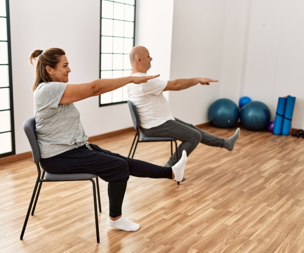 man and woman doing exercises on chairs in a gym