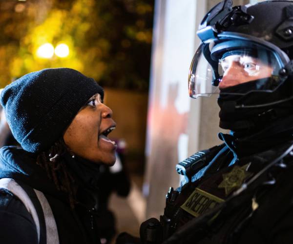 woman shouts in the face of a police officer in riot gear