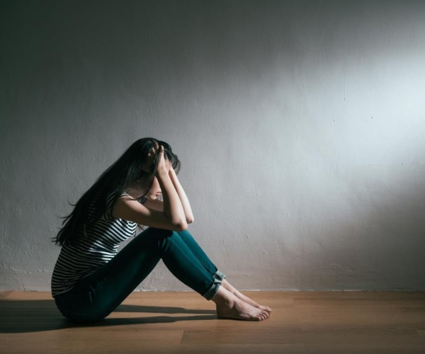 young girl sitting on floor in room feeling sad