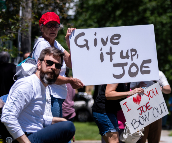 protesters holding signs saying they love biden but urge him to quit the reace