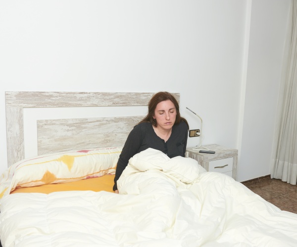 woman with eyes closed sitting up in bed just after waking up