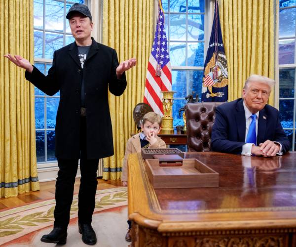 musk gestures as he stands and speaks next to trump seated at his oval office desk as a boy stands next to the desk