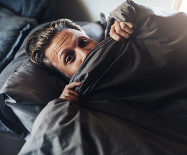 man in bed with covers up to his nose looking scared