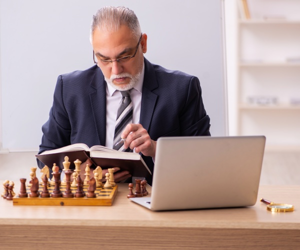 man reading a book and playing chess and looking at laptop