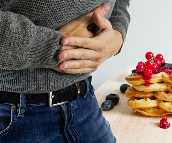 man holding stomach in pain, plate of waffles, fruit next to him