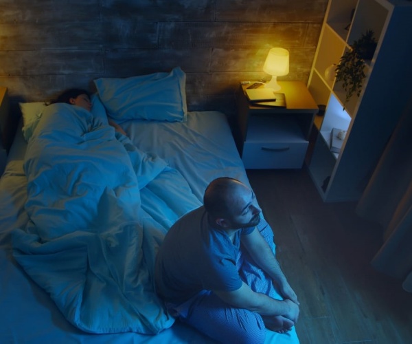 man sitting up awake on a messy bed in middle of night