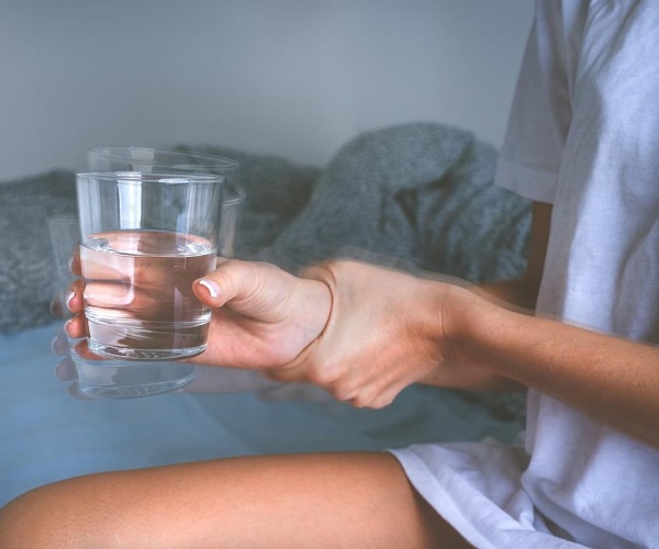 woman holding her hand steady as she holds glass of water