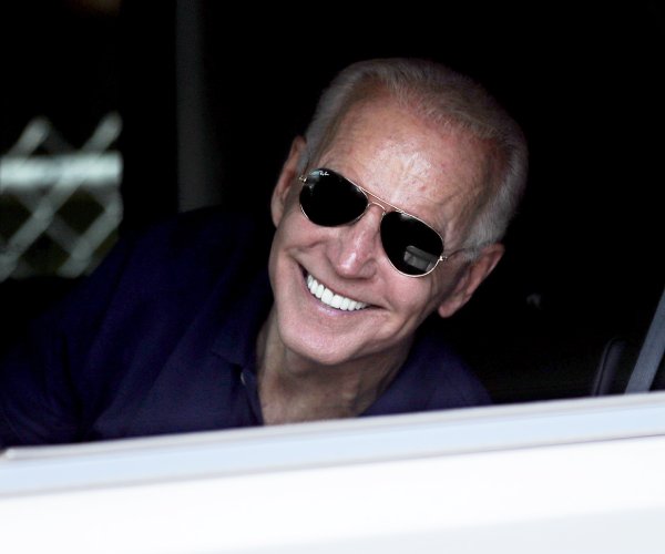 president joe biden smiling while looking out a car window