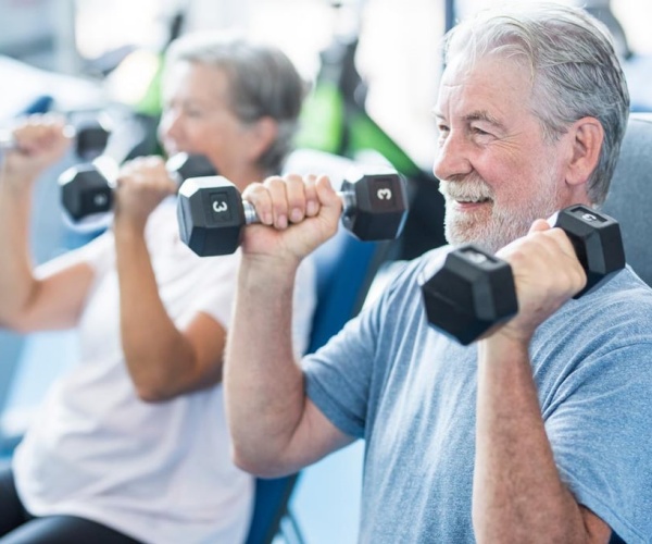 older man and woman at gym lifting weights