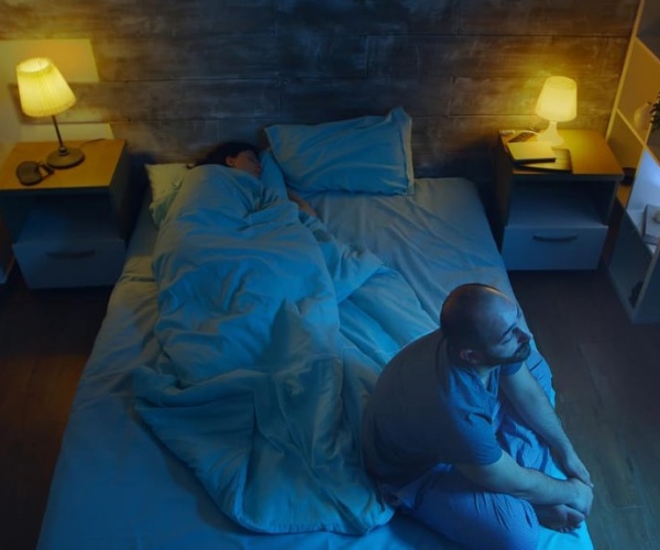 bedroom at night with side table lamps on and man awake, woman asleep