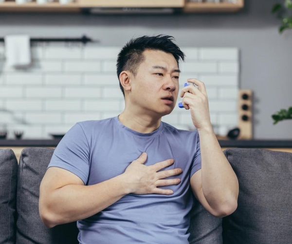 man sitting on couch using an inhaler