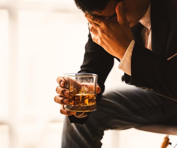 man with head in hands and holding a glass with liquor in it