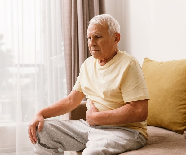 an elderly man sitting on a bed clutching his stomach