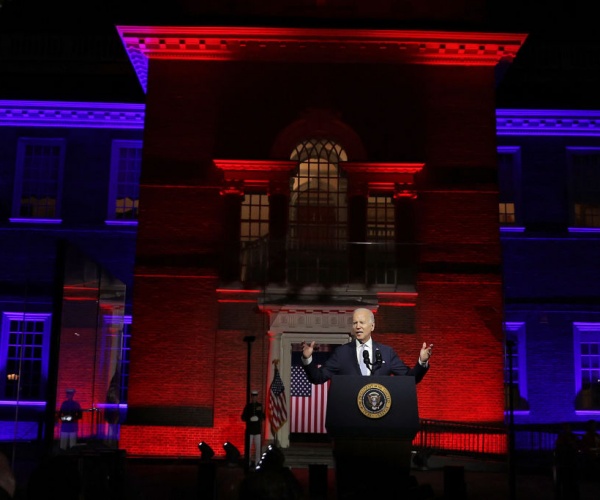 president biden delivers speech and gestures with hand with red and blue lights in background