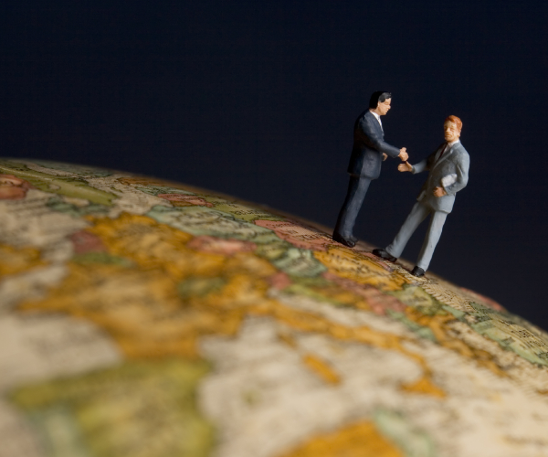 figurines of two businessmen shaking hands on a globe 