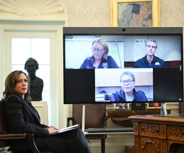 kamala harris sitting beside a monitor with three people on the screen