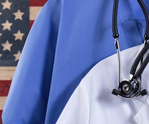 a man in medical scrubs with a stethoscope around his neck standing in front of an american flag