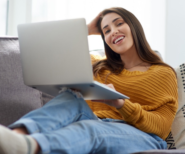 woman smiling at home laying on couch with laptop