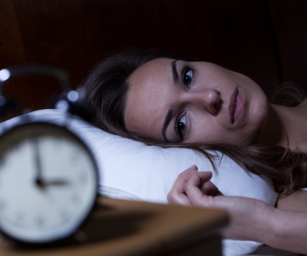 a woman lying in bed awake watches a clock