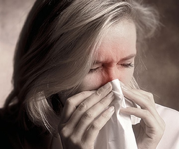 woman feeling miserable and blowing her red nose