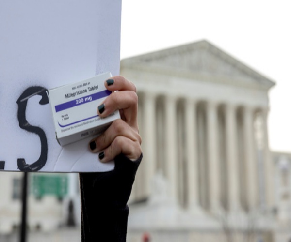 protestor in Washington DC holding sign and a box of mifepristone