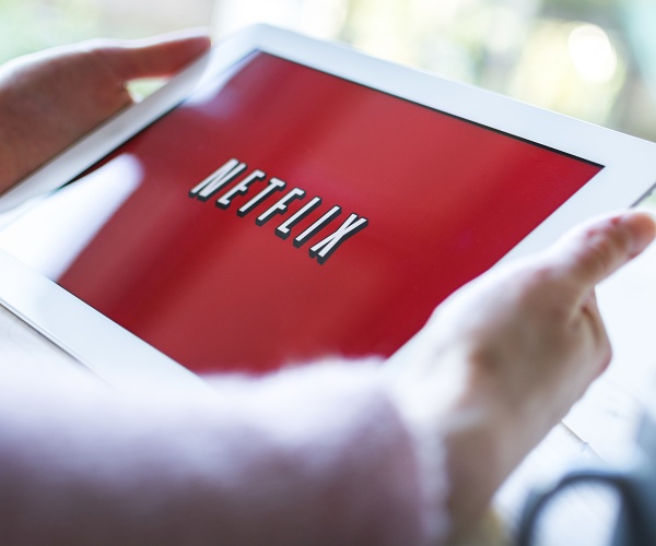 person holds tablet showing netflix logo on red background