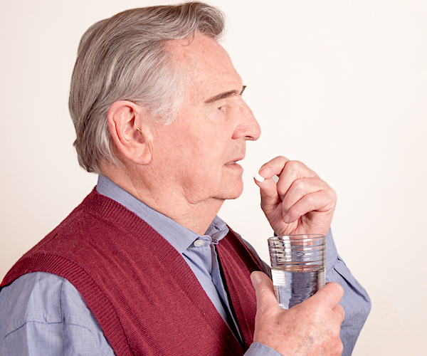 Portrait of senior man taking pill with glass of water isolated