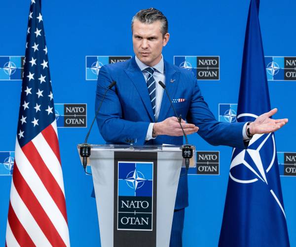 hegseth standing between american and nato flags