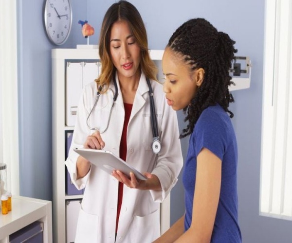 doctor talks to young woman about her health while looking at iPad