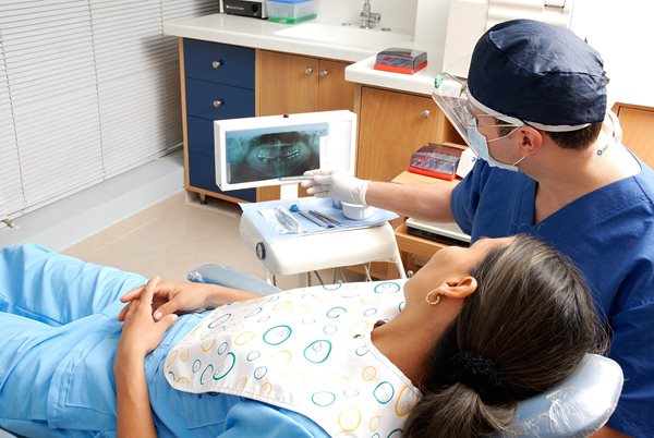 patient in chair in dentist's office with dentist looking at x-rays