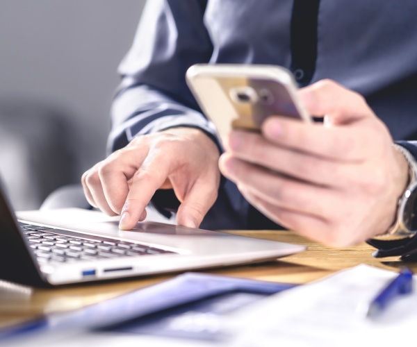 man on laptop, looking at smartphone