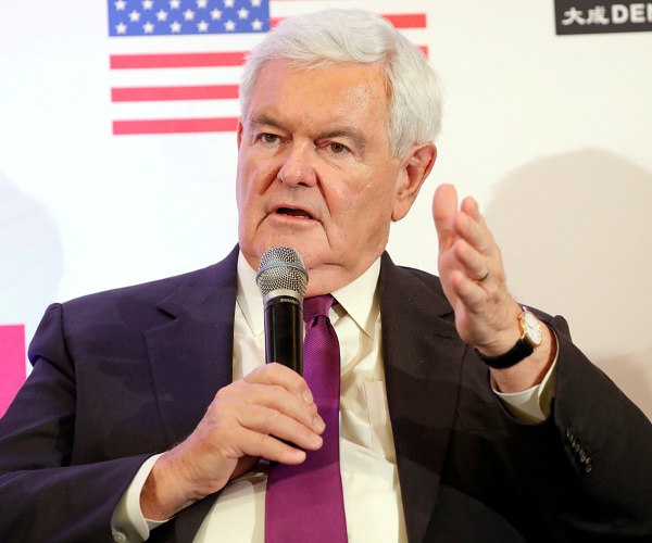 newt gingrich sits onstage and speaks into microphone