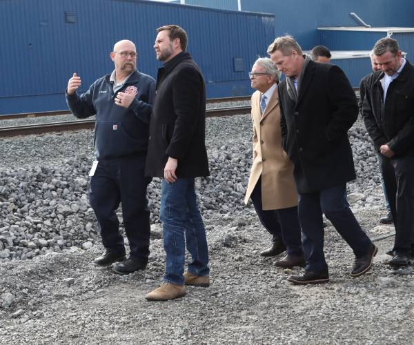 vance and a group of officials walk near a railroad track