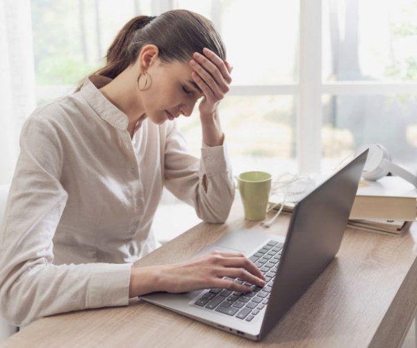 woman at desk on computer holding head in pain