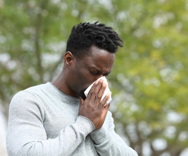 man sneezing outside near trees