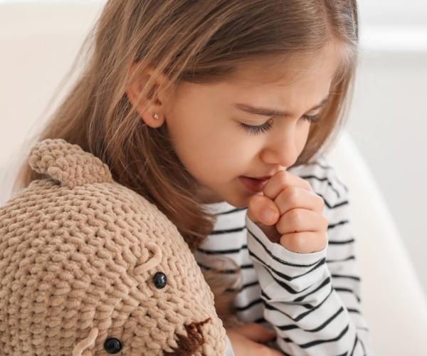 young girl holding teddy bear and covering mouth for a cough