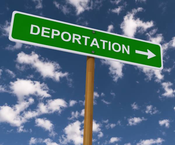 highway sign with deportation and a directional arrow against sky with clouds.
