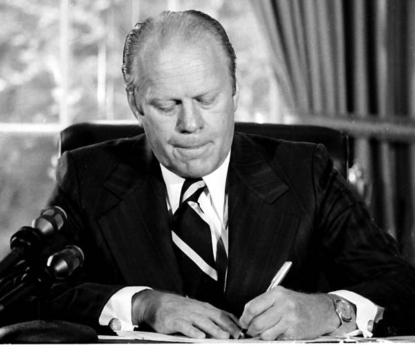 ford sitting at a desk signing a document