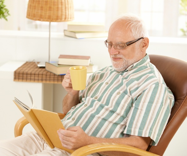 older man at home drinking tea, reading a book
