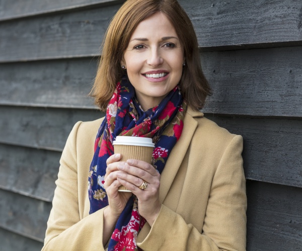 smiling woman outside with winter coat drinking a to-go coffee