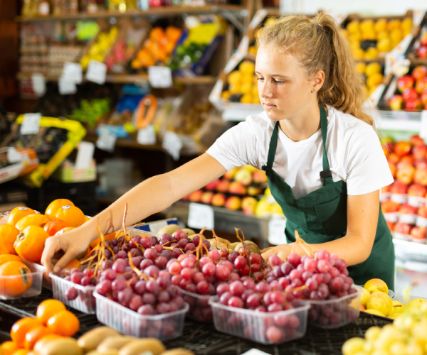 a teenage girl working in grocery store selling fresh grapes in the produce department