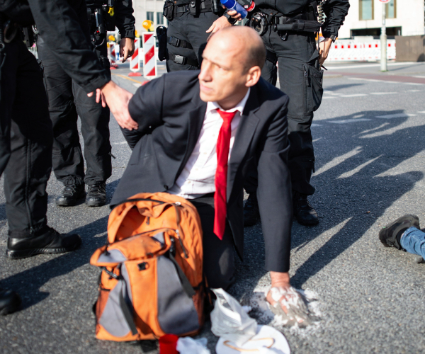 police behind a man in a suit with his hand glued to the street