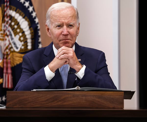 joe biden sits at a desk with his hands clasped