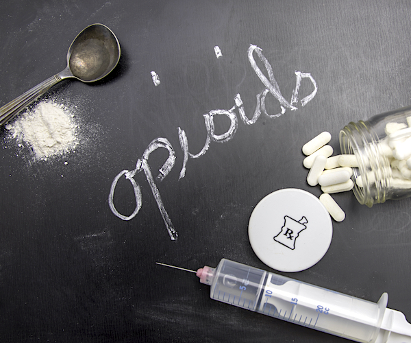 Opioids written in chalk on blackboard with crushed powder, spoon, syringe and prescription vial