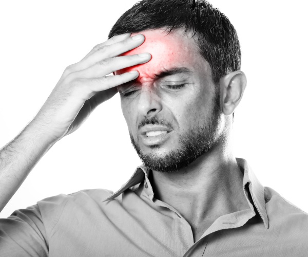 man with migraine holding his forehead, highlighted in red, in pain