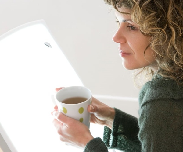 woman holding coffee in front of a light box for light therapy